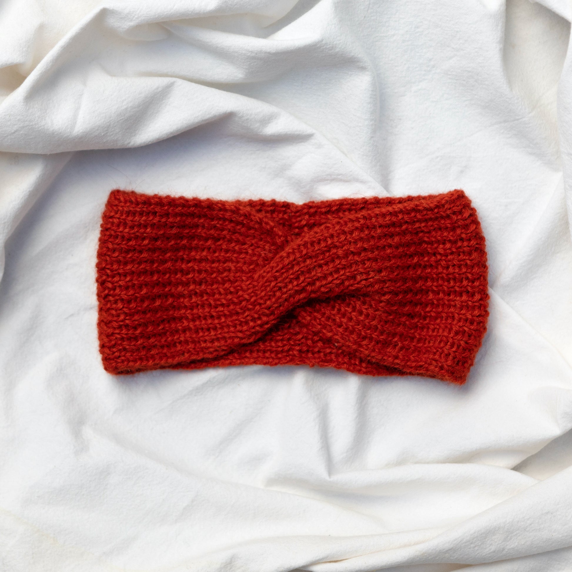 Cosy hand knitted orange coloured headband with a cute twist at the front