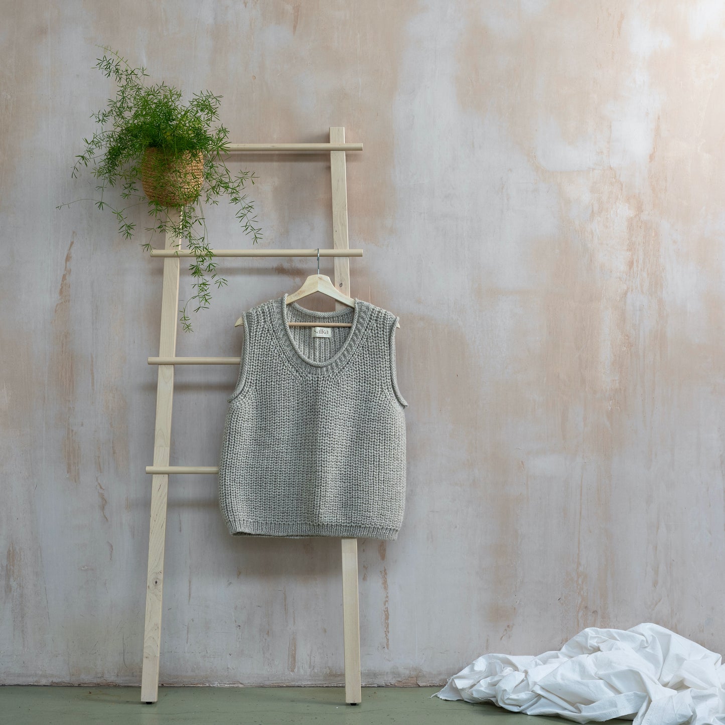Light grey highland wool hand knitted vest hanging on ladder
