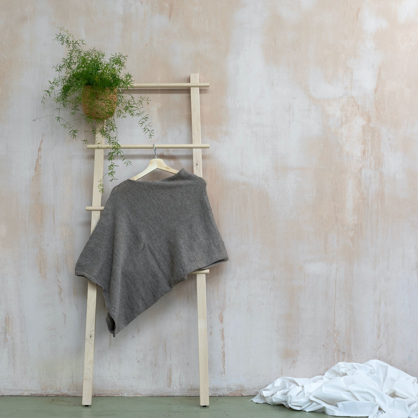 Asymmetrical beige luxury knitted poncho hanging on wooden ladder