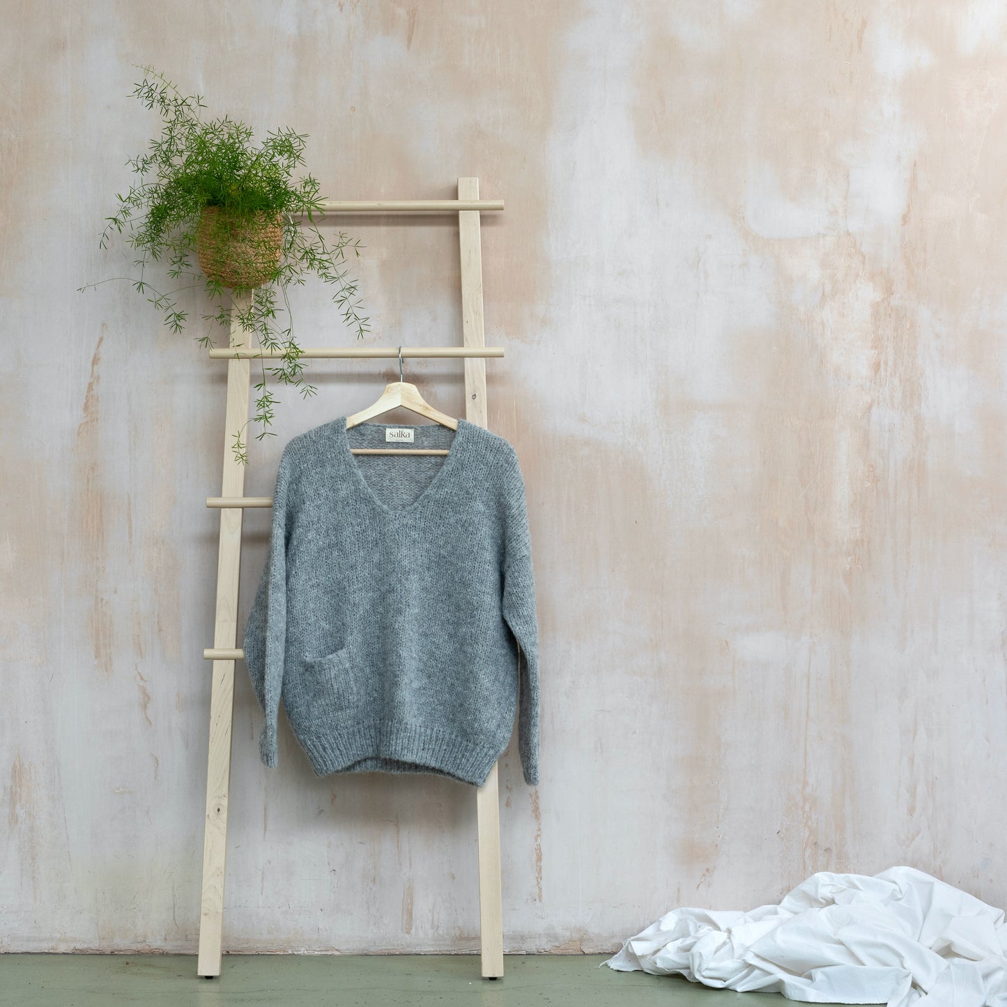 Warm v-neck alpaca sweater, light grey colour, displayed on a ladder