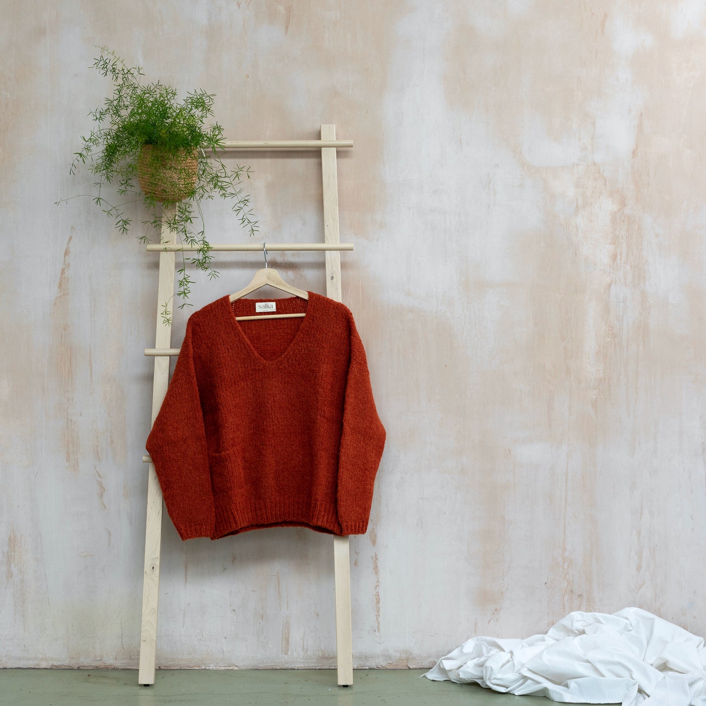 Warm v-neck sweater, alpaca wool, orange colour, displayed on a ladder
