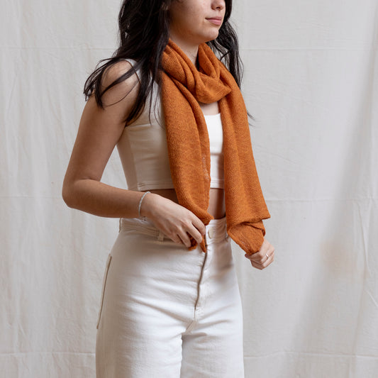 Woman wearing soft-orange coloured lightweight and delicately woven scarf. Hand-made by artisans.