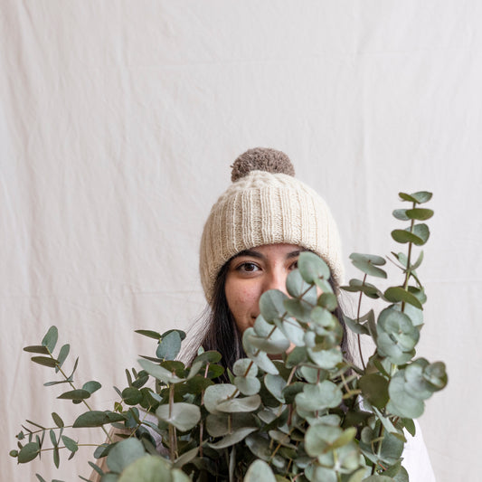 Woman wearing natural coloured hand-knitted cable beanie hat with pom pom