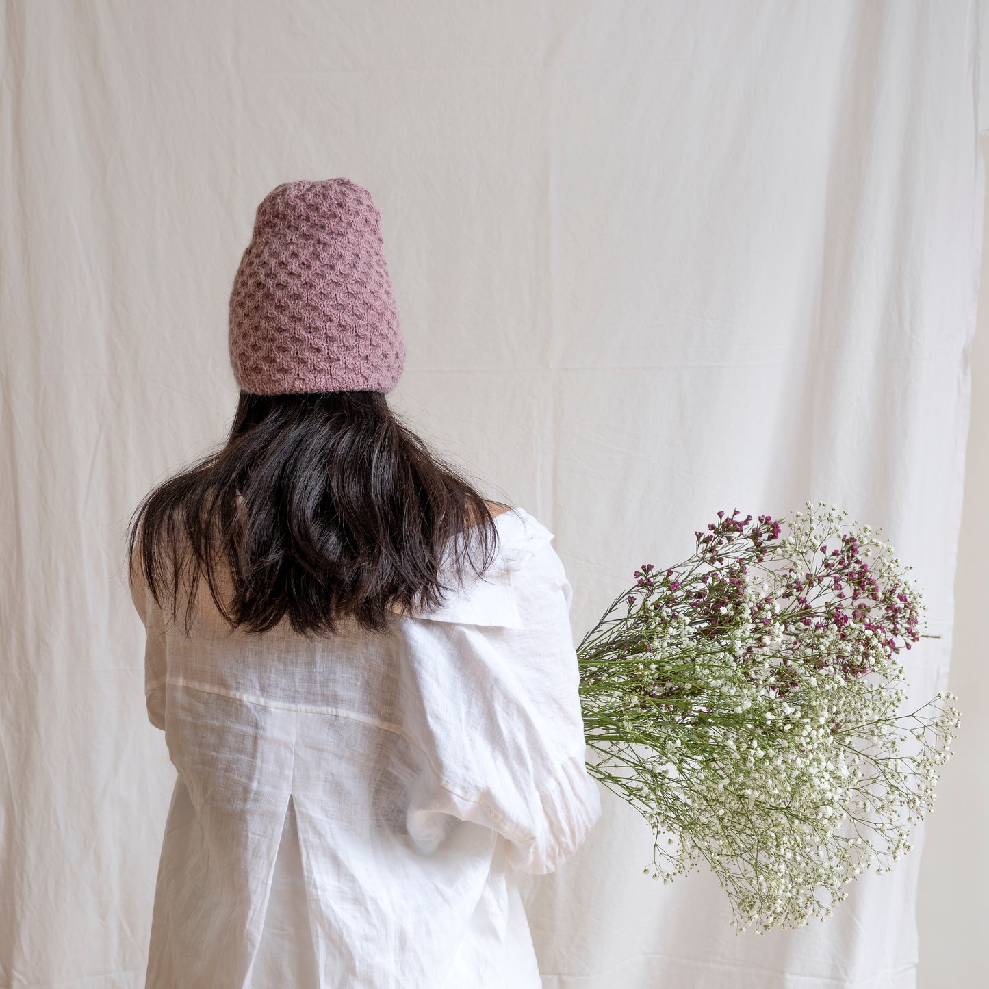Woman wearing textured hand-knitted rose-pink beanie hat.