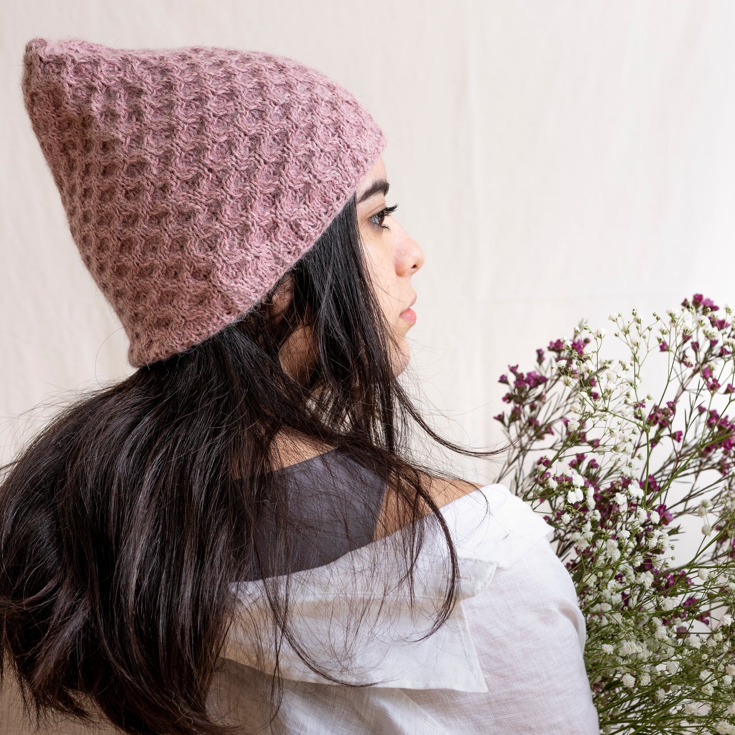 Woman wearing textured hand-knitted rose-pink beanie hat.