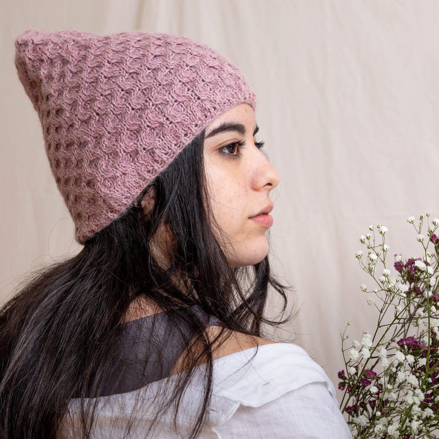 Woman wearing textured hand-knitted rose-pink beanie hat.