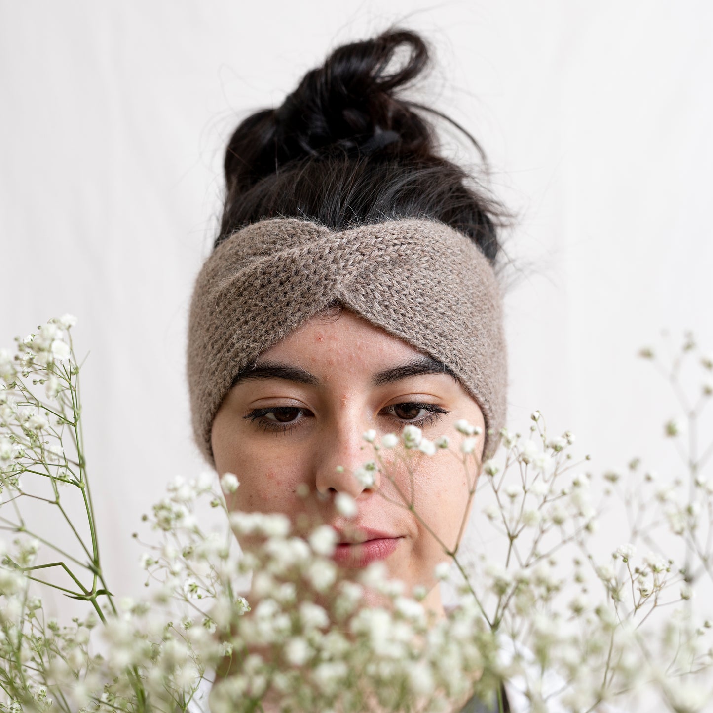 Woman wearing cosy hand-knitted oatmeal coloured headband with a cute twist at the front.