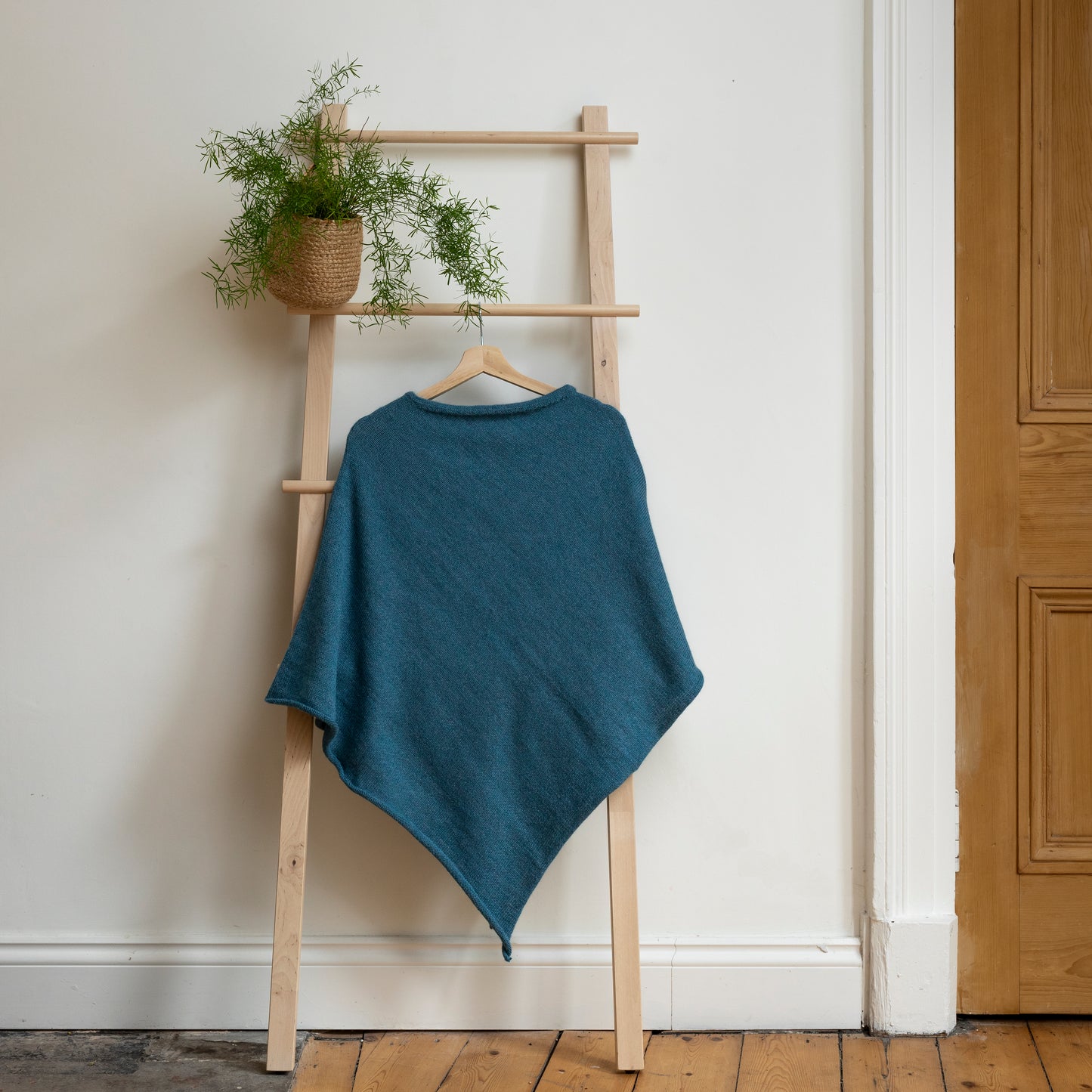 Lightweight texture and blue coloured, purely alpaca wool lightweight poncho hanging from wooden steps.