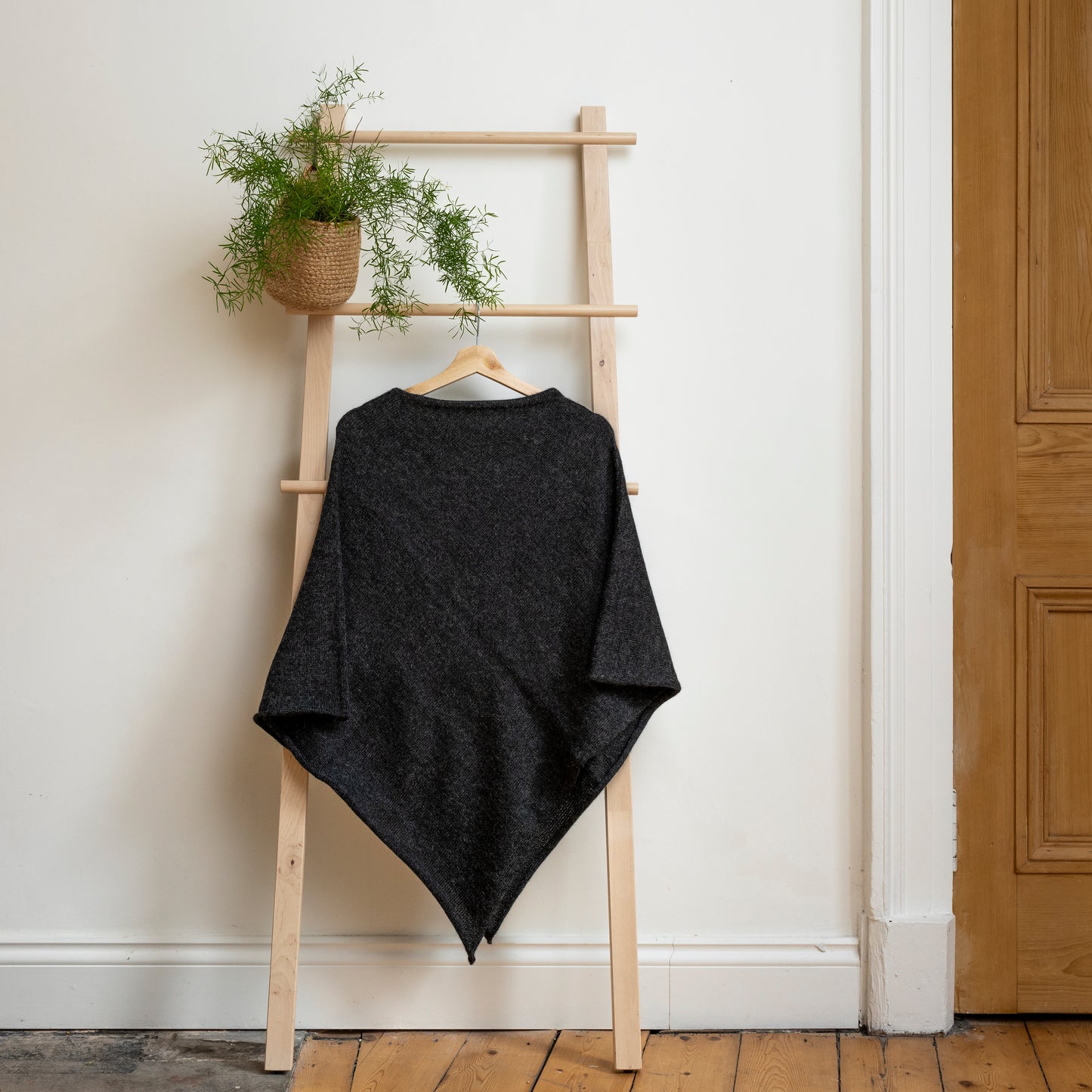 Lightweight texture and charcoal coloured, purely alpaca wool lightweight poncho hanging from wooden steps.
