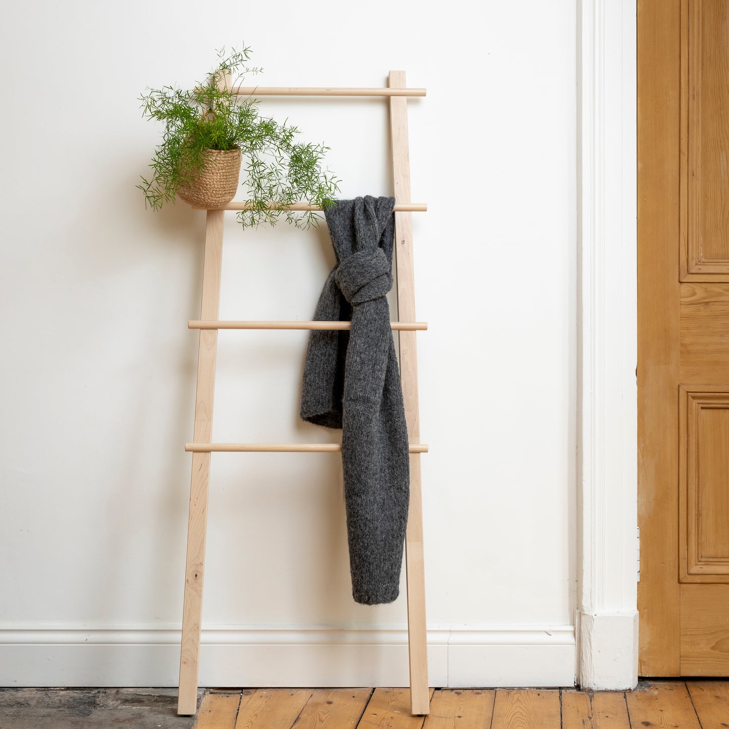 Chunky super-soft knitted scarf in colour charcoal hanging from wooden steps. 