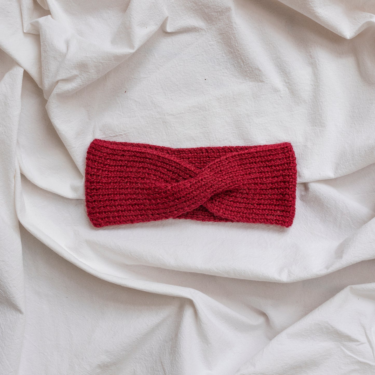 Cosy hand-knitted burgundy coloured headband with a cute twist at the front.