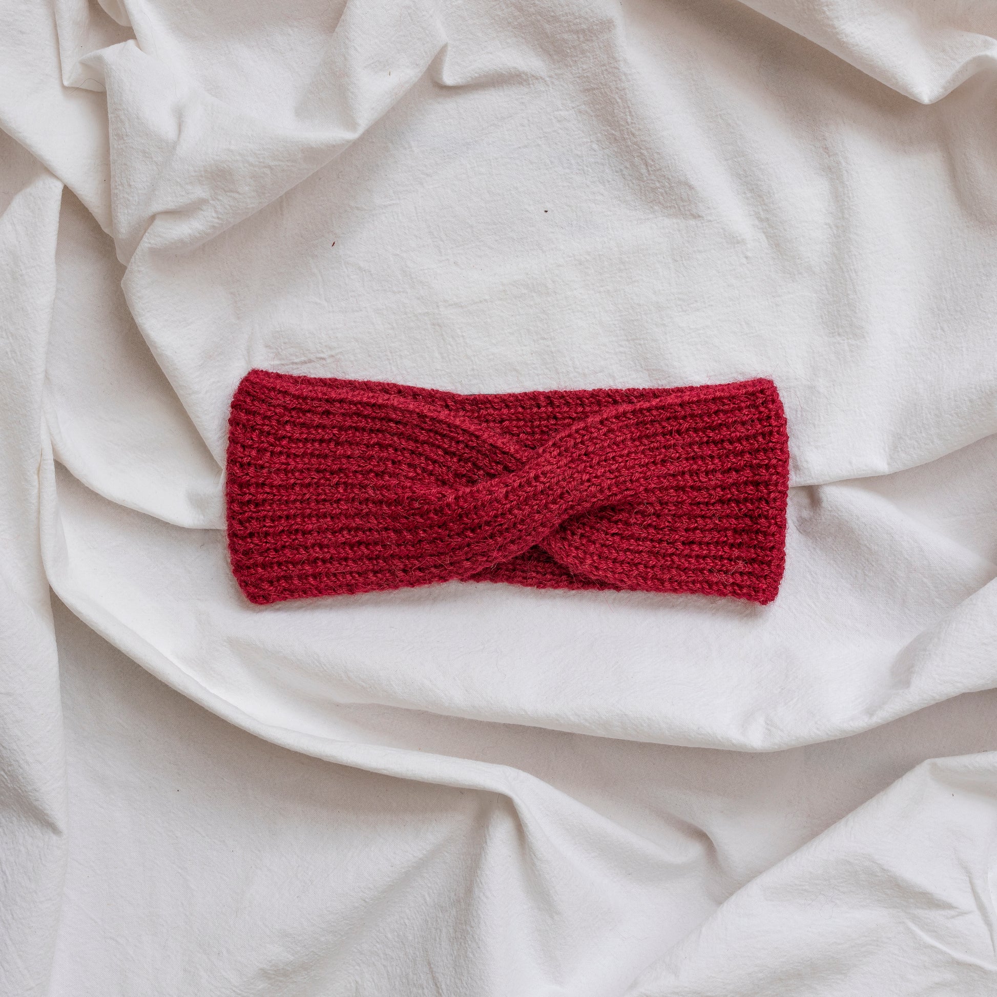 Cosy hand-knitted burgundy coloured headband with a cute twist at the front.