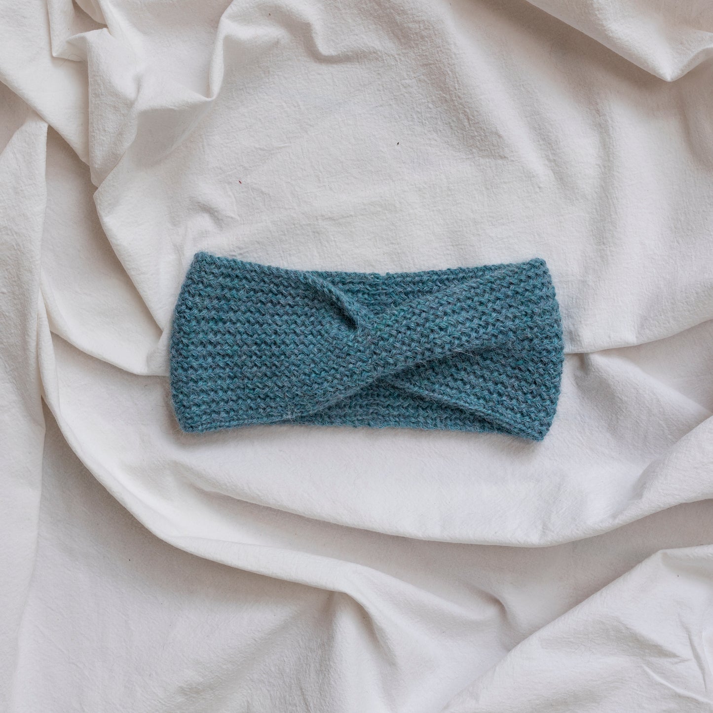 Cosy hand-knitted light blue coloured headband with a cute twist at the front.