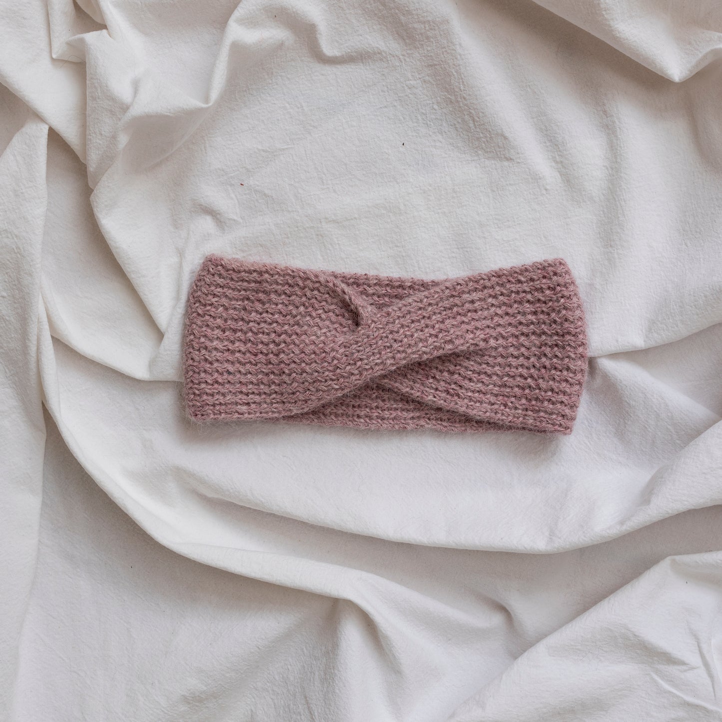 Cosy hand-knitted rose pink coloured headband with a cute twist at the front.