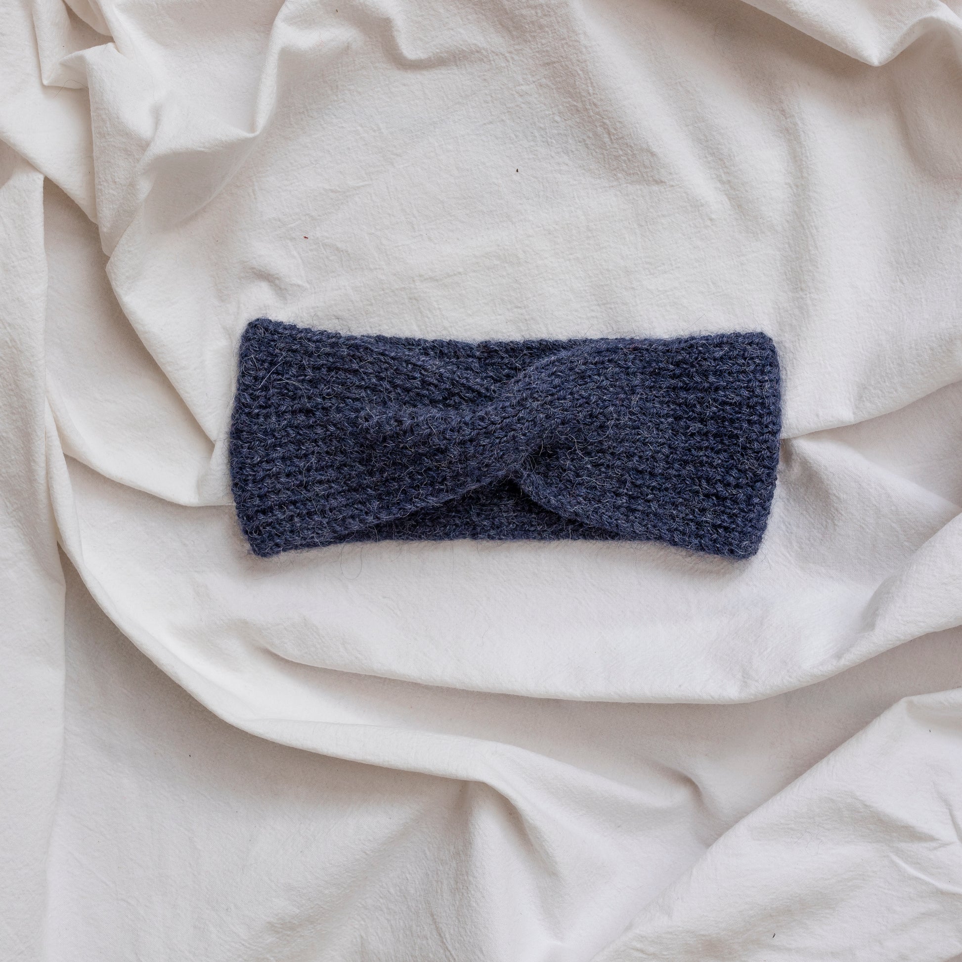 Cosy hand-knitted dark blue coloured headband with a cute twist at the front.