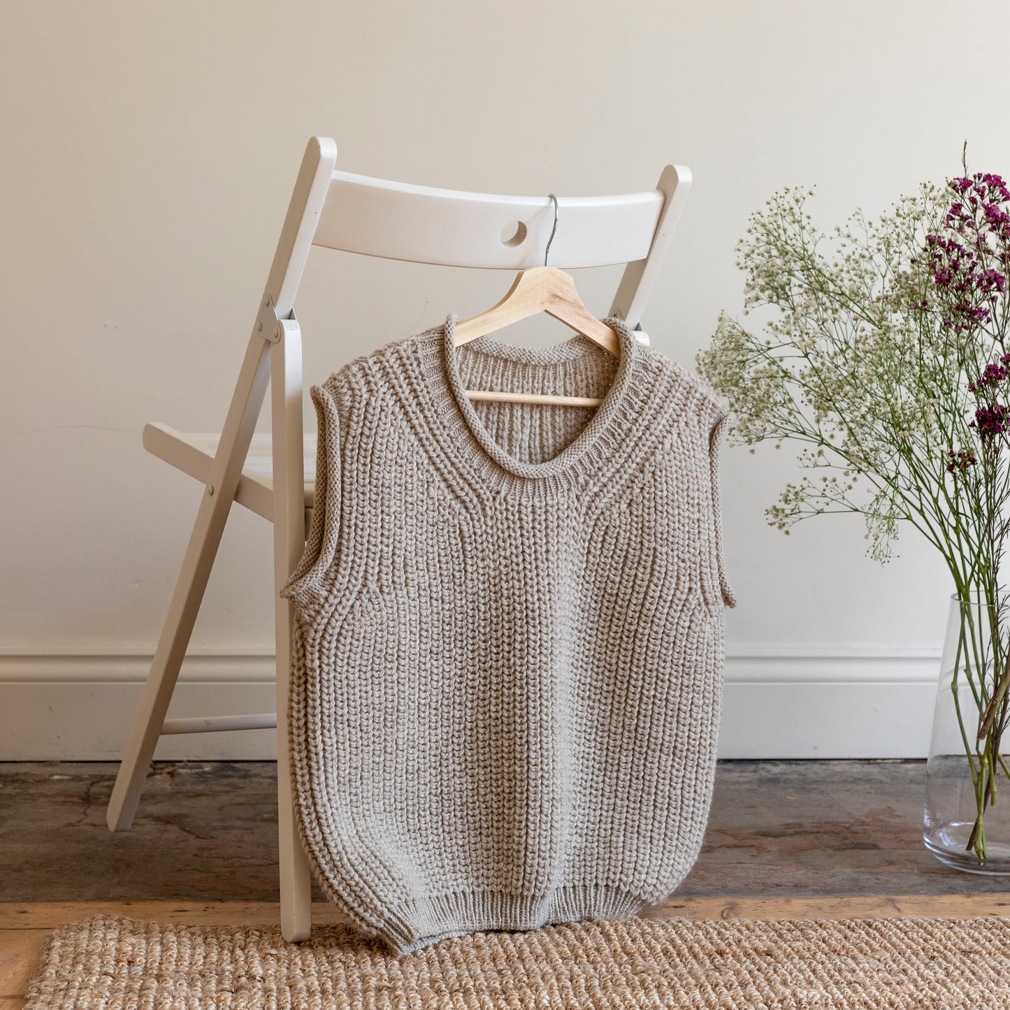 Luxury alpaca wool hand-knitted vest hanging on the back of white wooden chair.