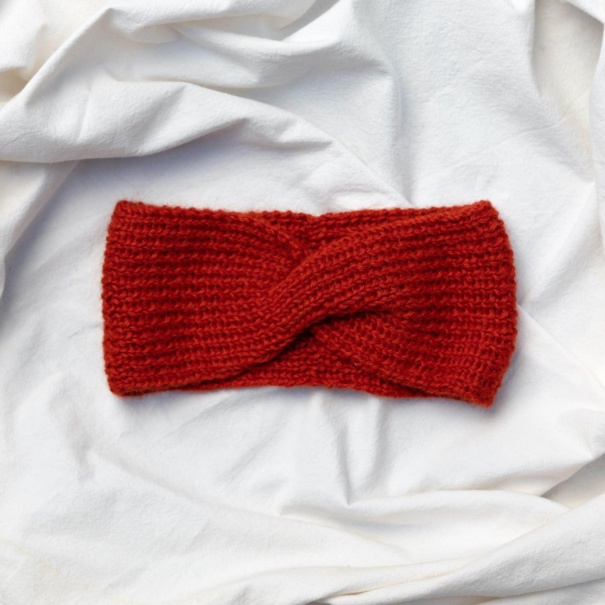 Cosy hand knitted orange coloured headband with a cute twist at the front 
