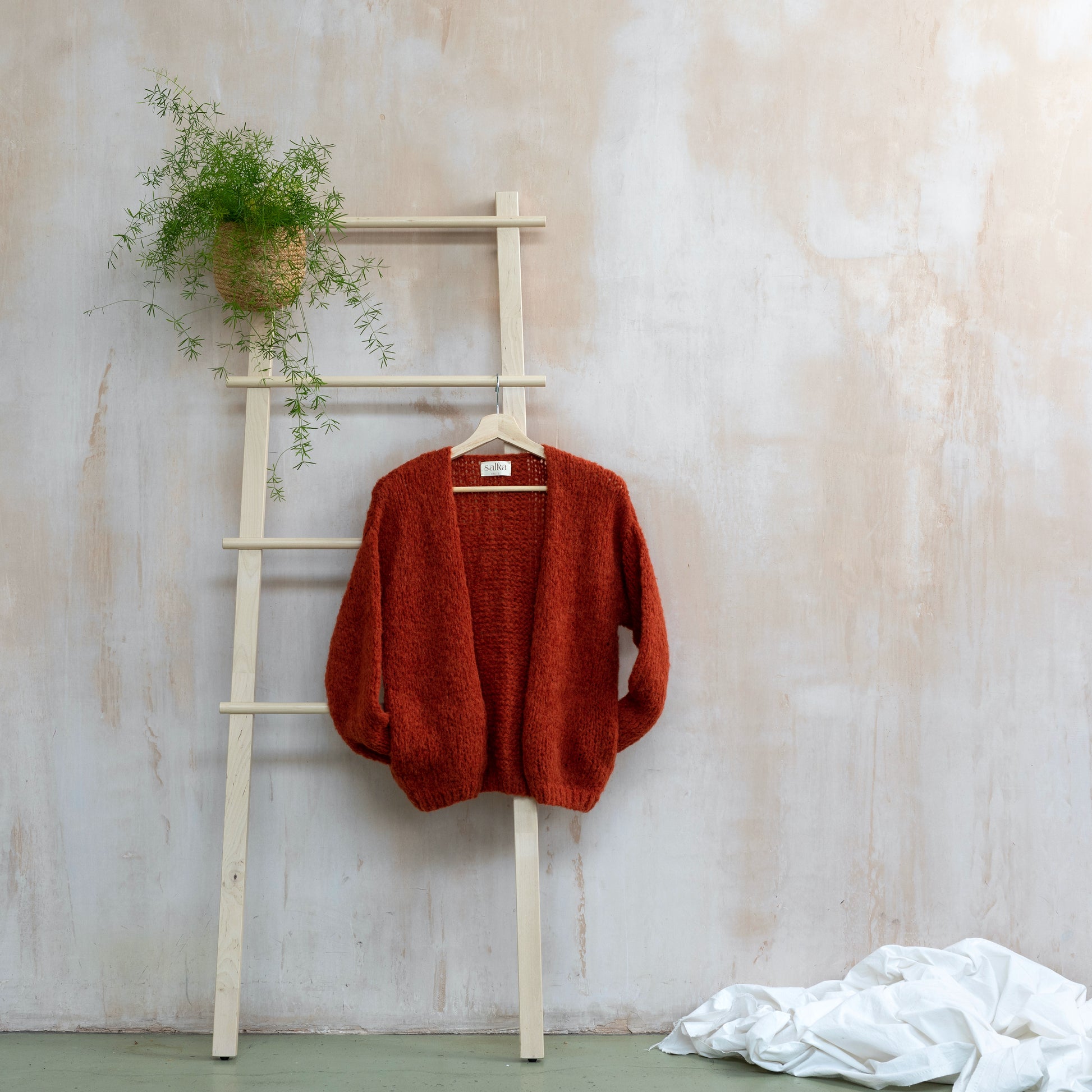Orange coloured knitted alpaca wool cardigan hanging on wooden ladder. Super soft and cosy