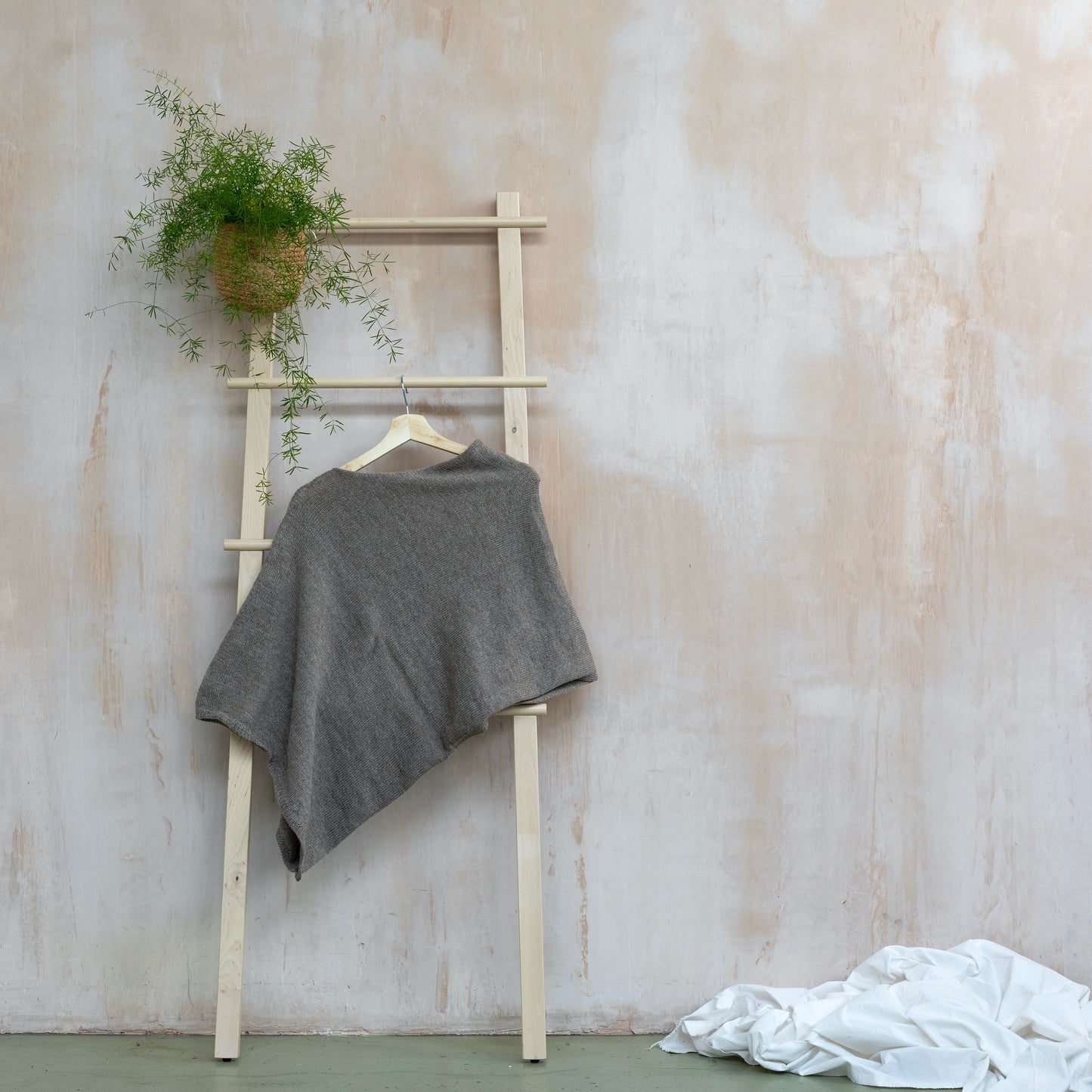 Asymmetrical beige luxury knitted poncho hanging on wooden ladder 