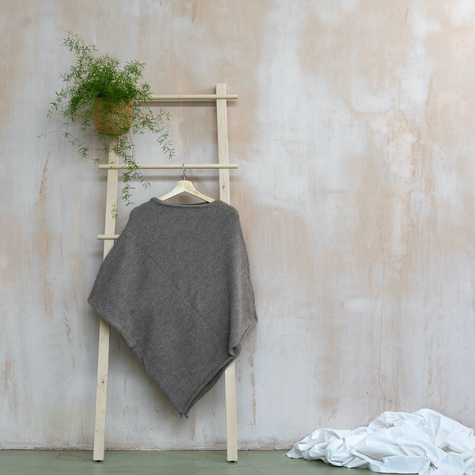 Beige coloured lightweight pure alpaca wool poncho hanging from wooden ladder 