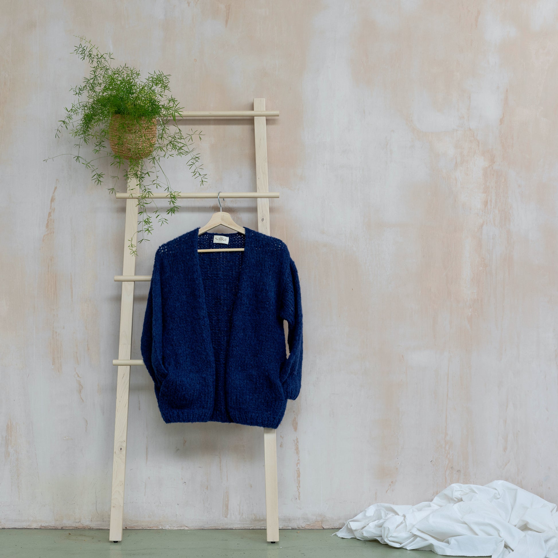 Dark navy coloured knitted alpaca wool cardigan hanging on wooden steps. Beautiful-one-of-a-kind item