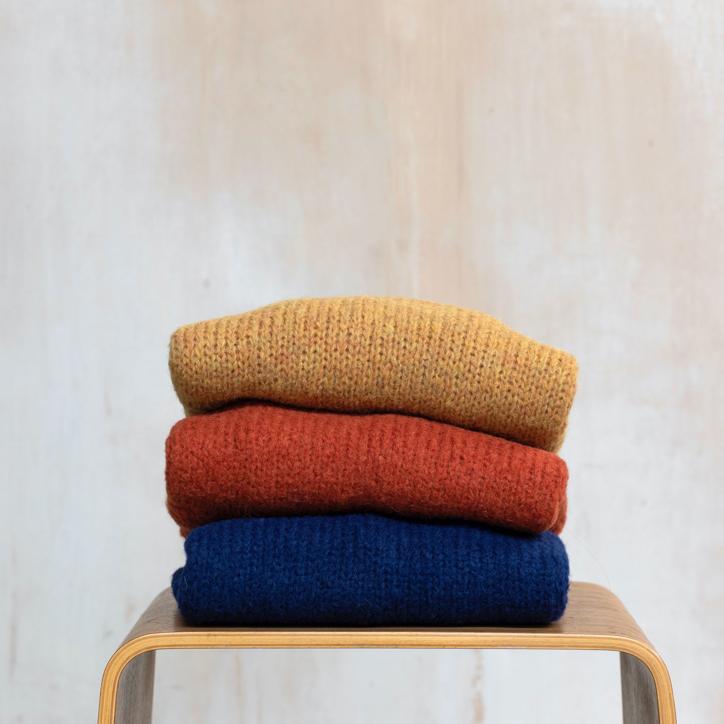 Three alpaca sweaters folded on a chair, yellow, orange and navy blue 