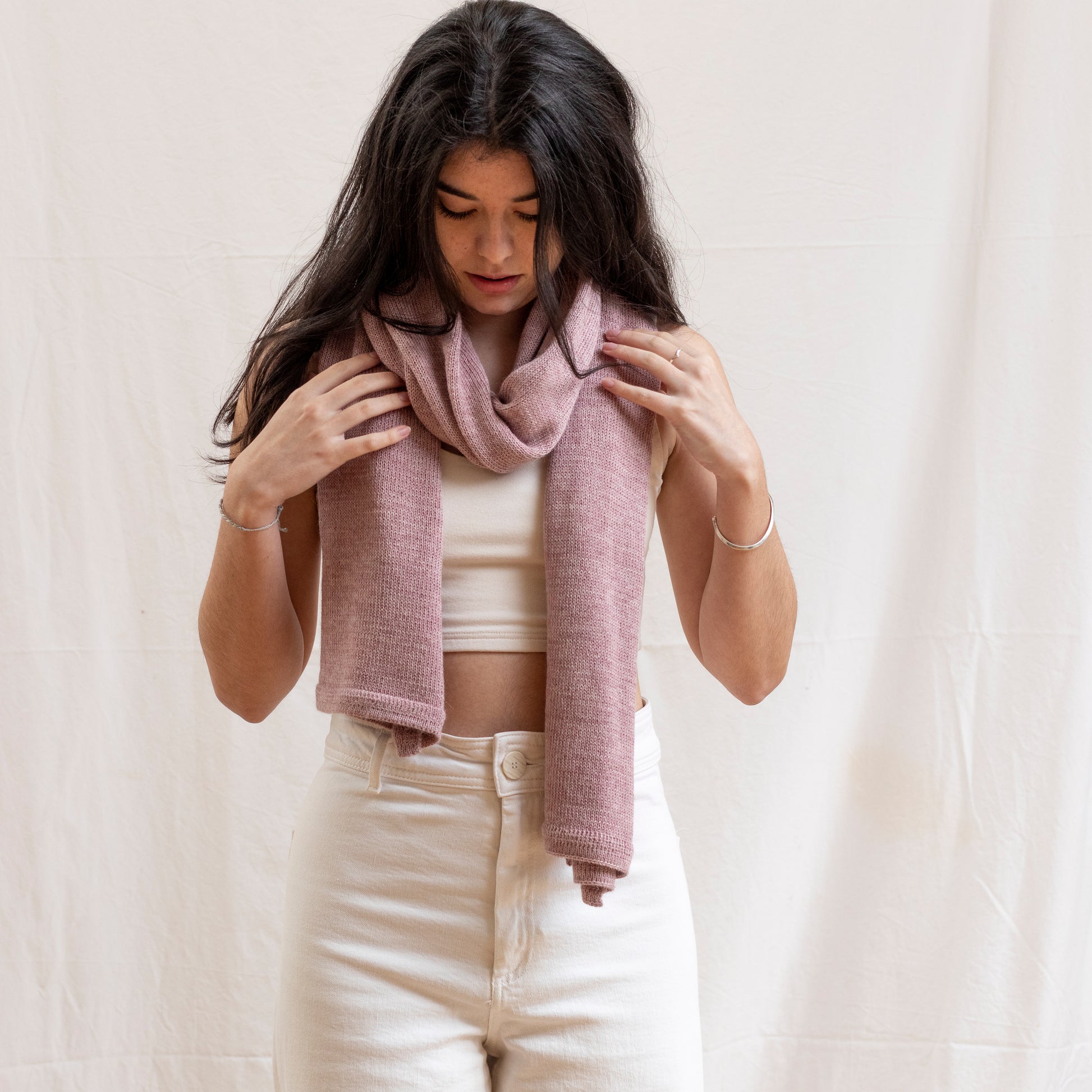 Woman wearing a luxurious alpaca wool one-of-a-kind pink scarf, hand-knitted by artisans. 