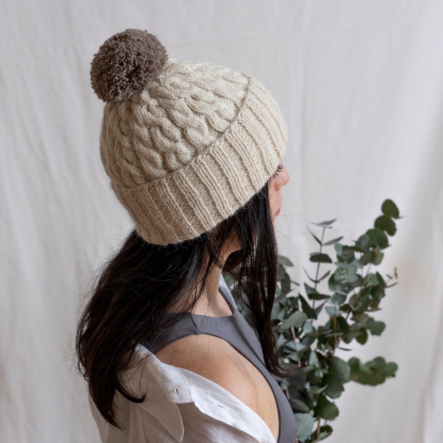 Woman wearing natural coloured hand-knitted cable beanie hat with pom pom