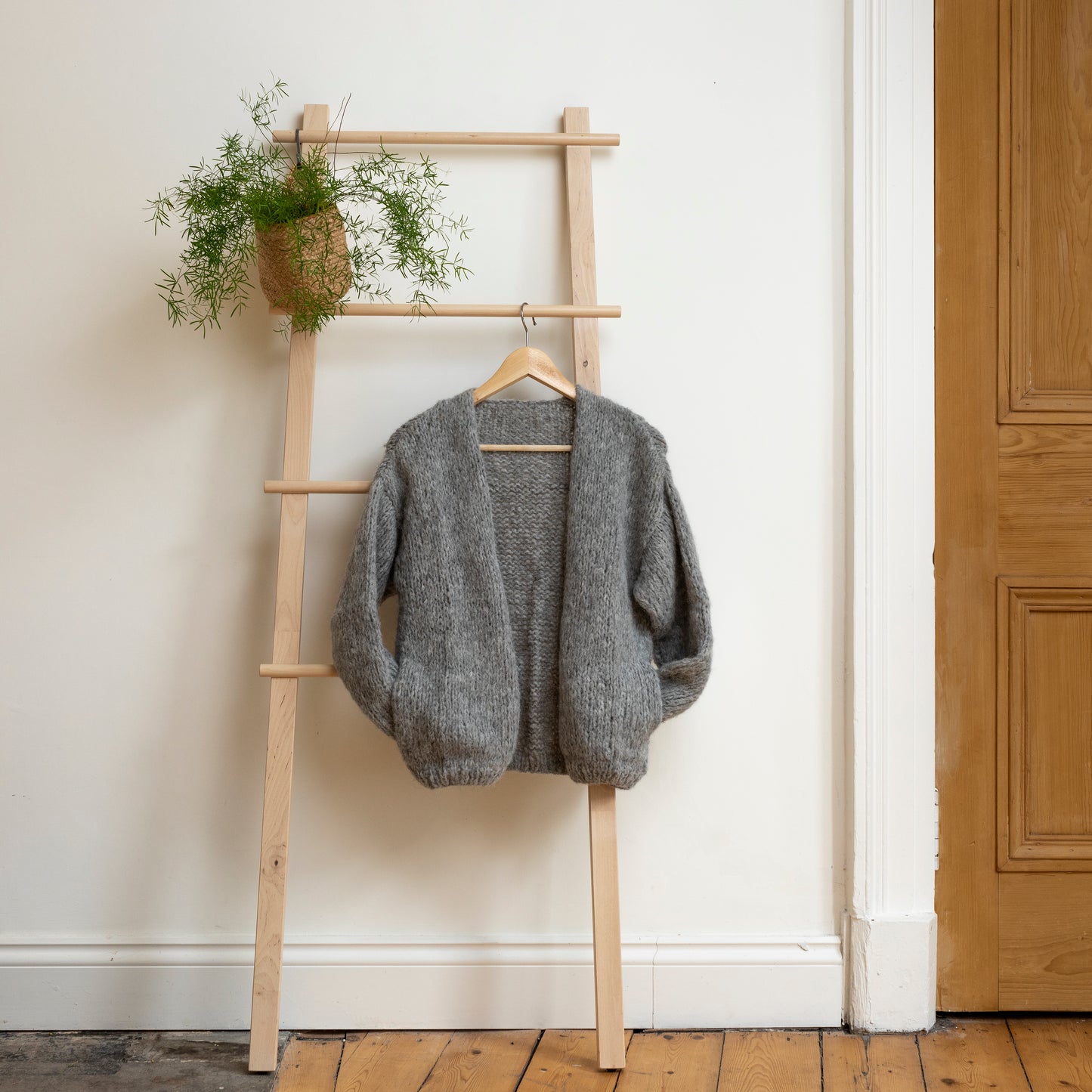 Soft grey coloured knitted alpaca wool cardigan hanging on wooden steps. Beautiful one-of-a-kind item.