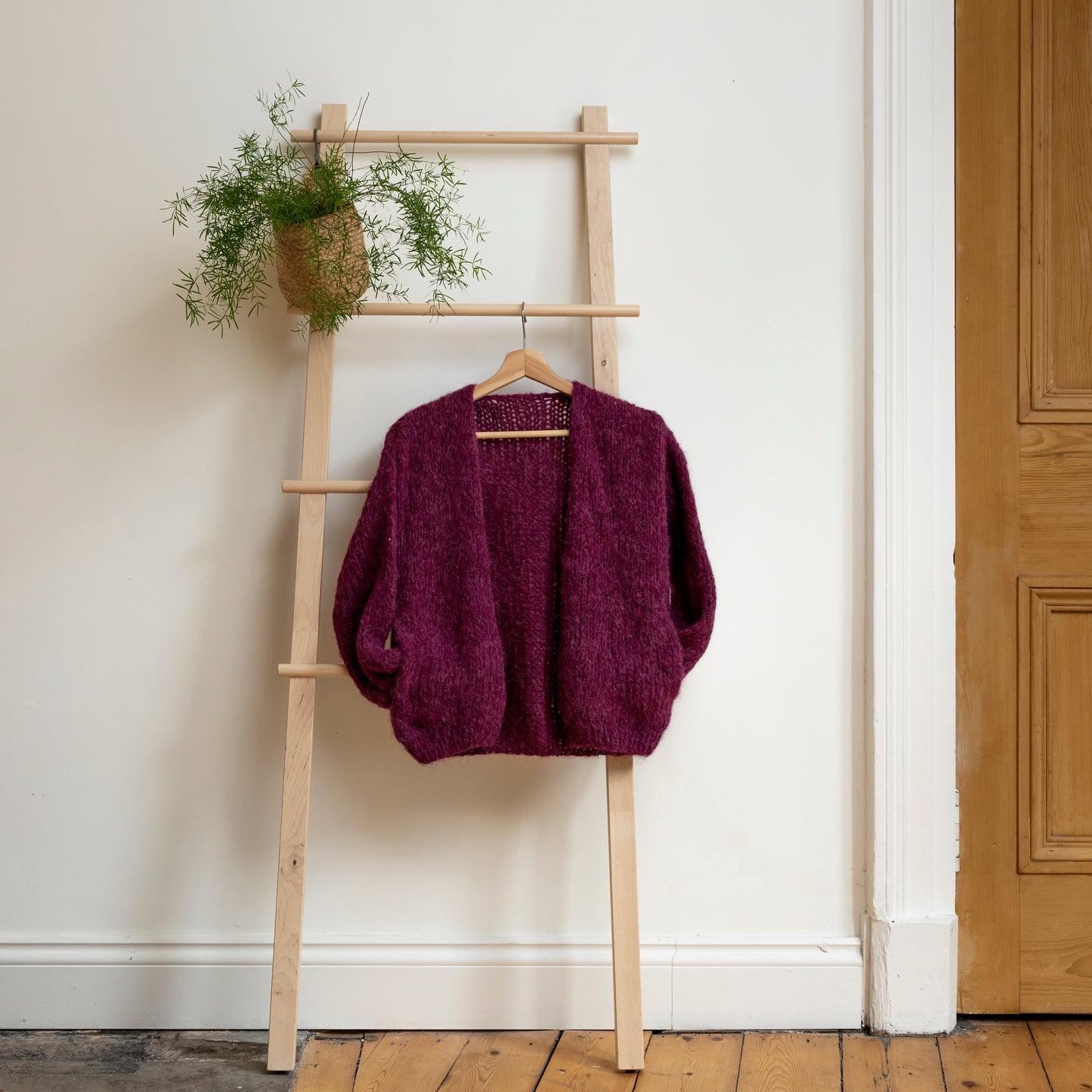 Plum coloured knitted alpaca wool cardigan hanging on wooden steps. Beautiful one-of-a-kind item.
