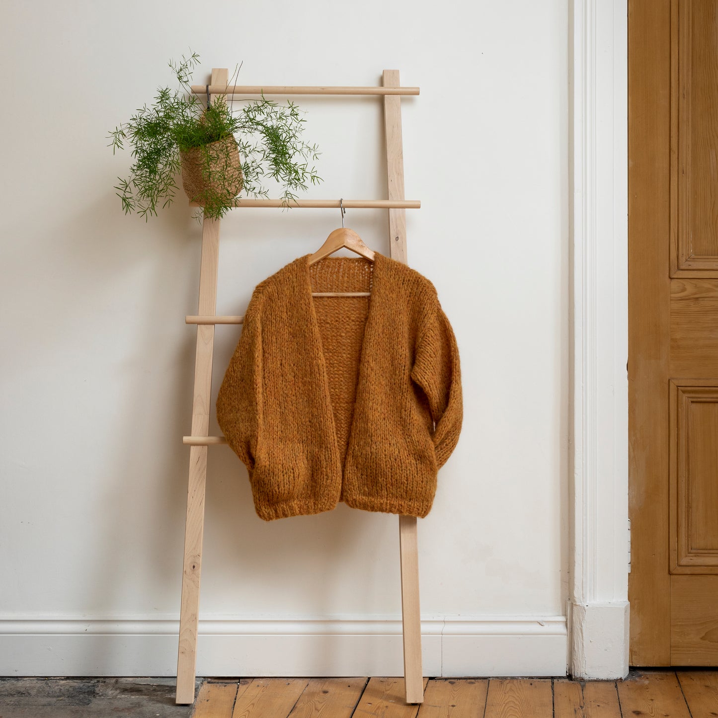 Yellow coloured knitted alpaca wool cardigan hanging on wooden steps. Beautiful one-of-a-kind item.