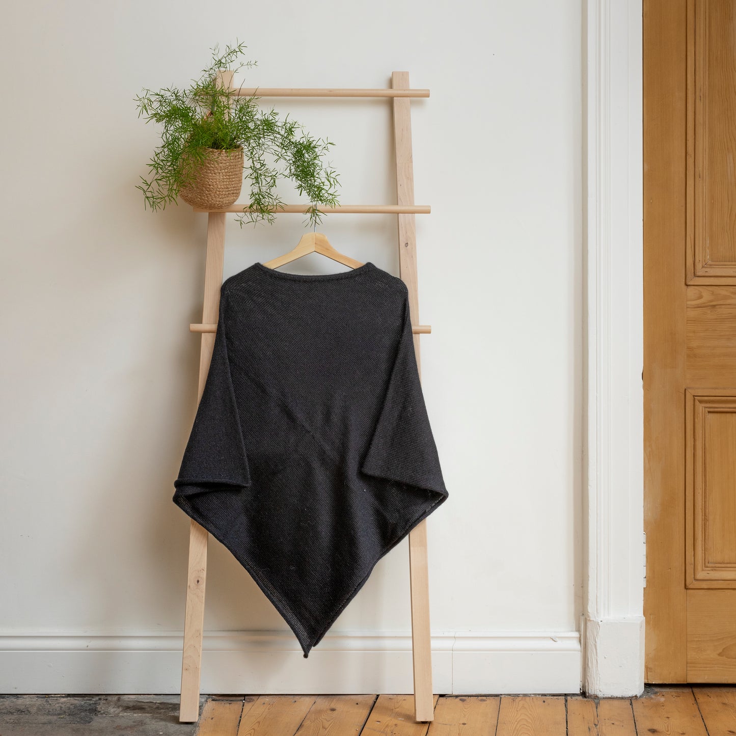 Lightweight texture and charcoal coloured, purely alpaca wool lightweight poncho hanging from wooden steps.