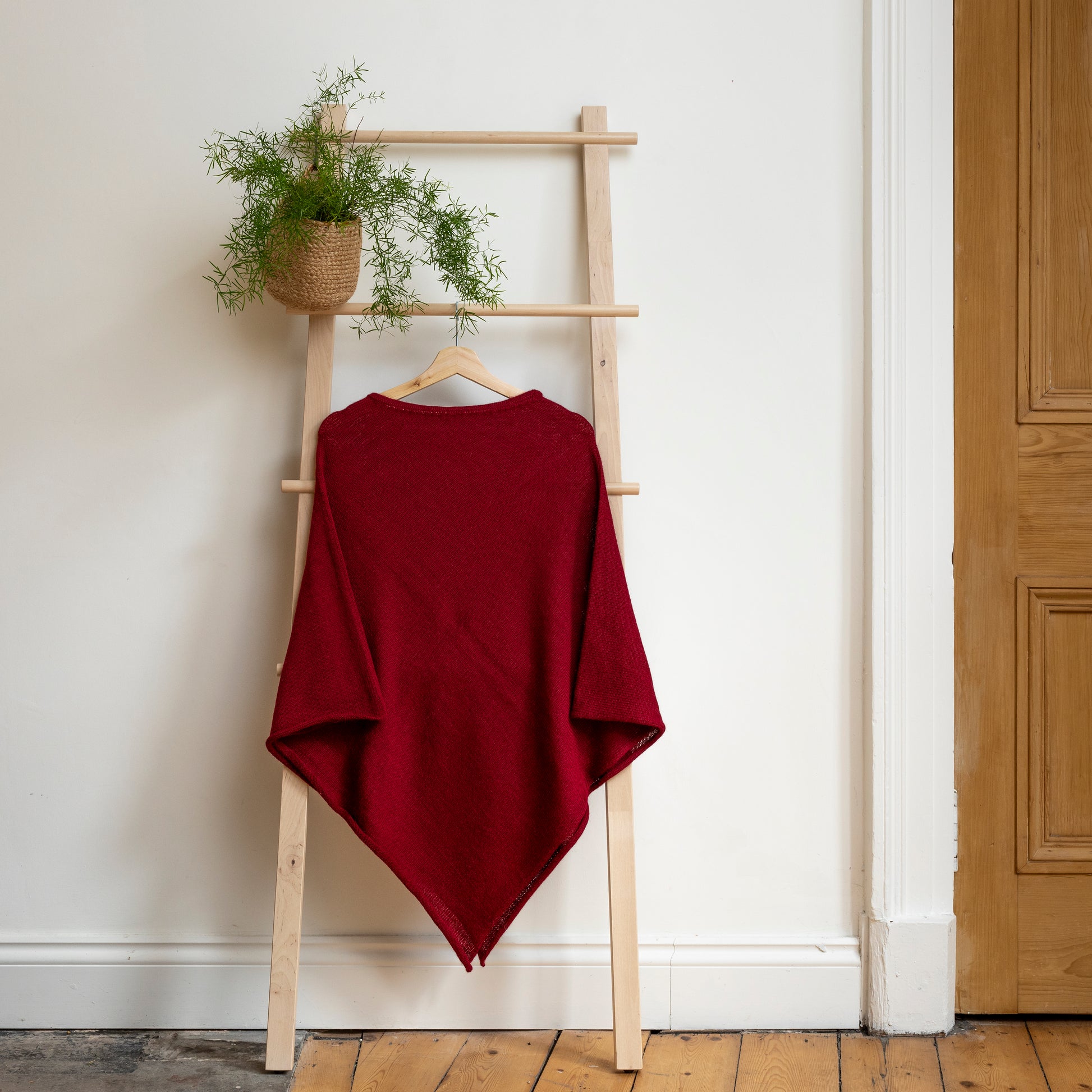 Lightweight texture and burdundy coloured, purely alpaca wool lightweight poncho hanging from wooden steps.