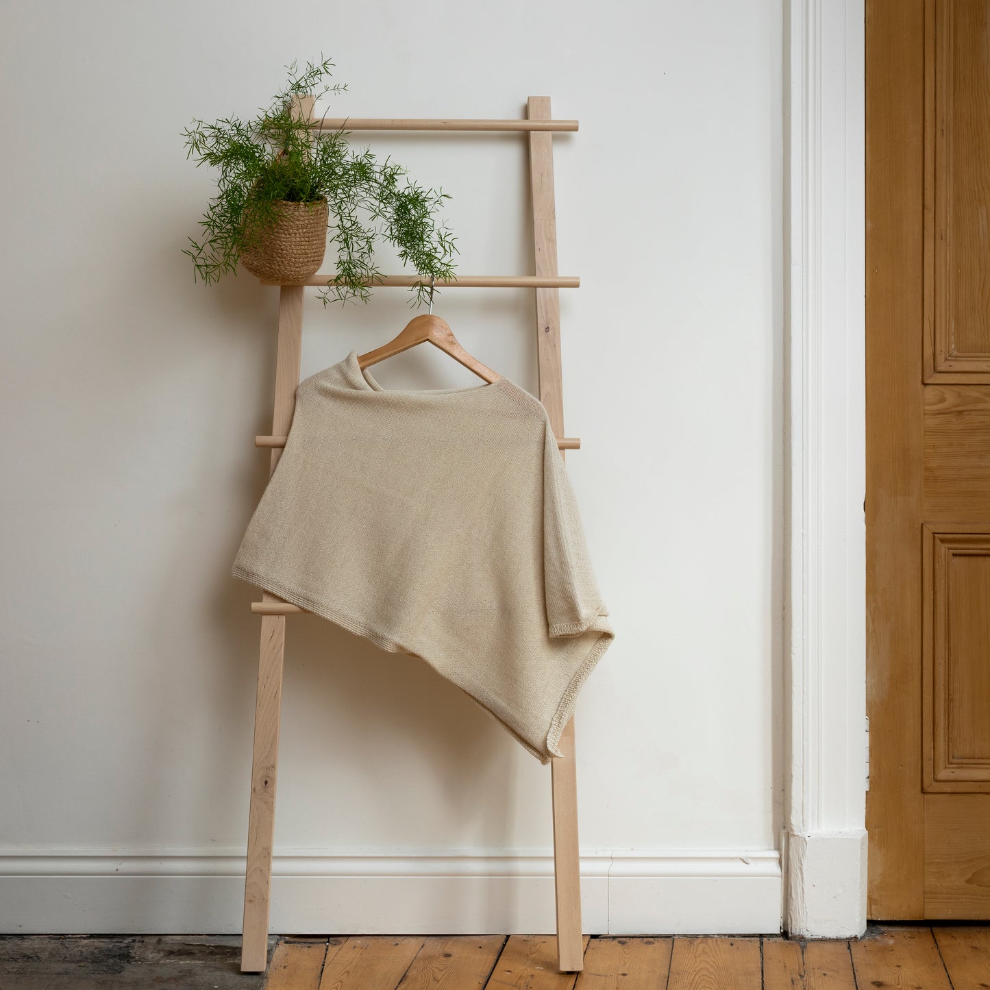 Asymmetrical natural coloured luxury knitted poncho hanging on wooden ladder.