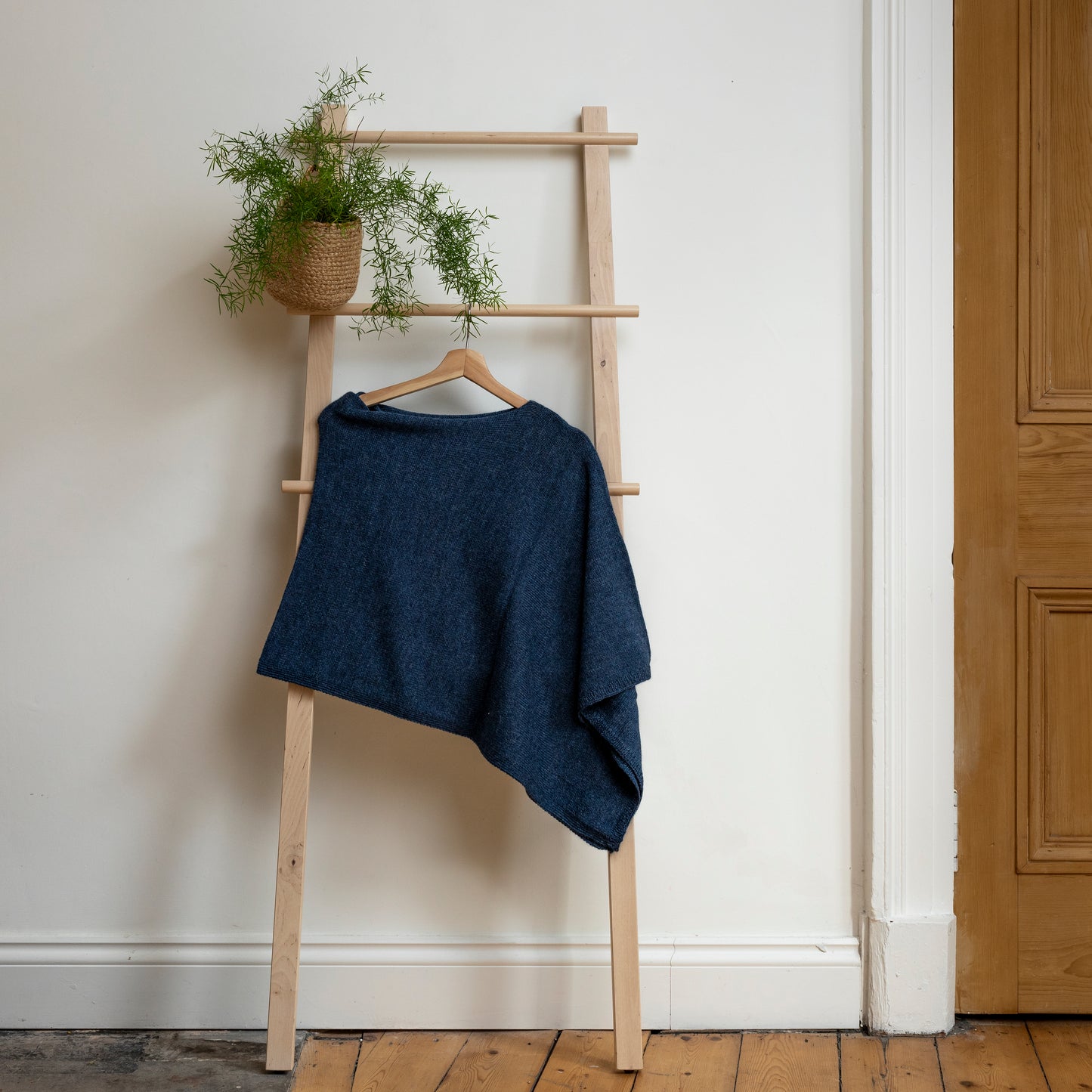 Asymmetrical dark blue luxury knitted poncho hanging on wooden ladder.