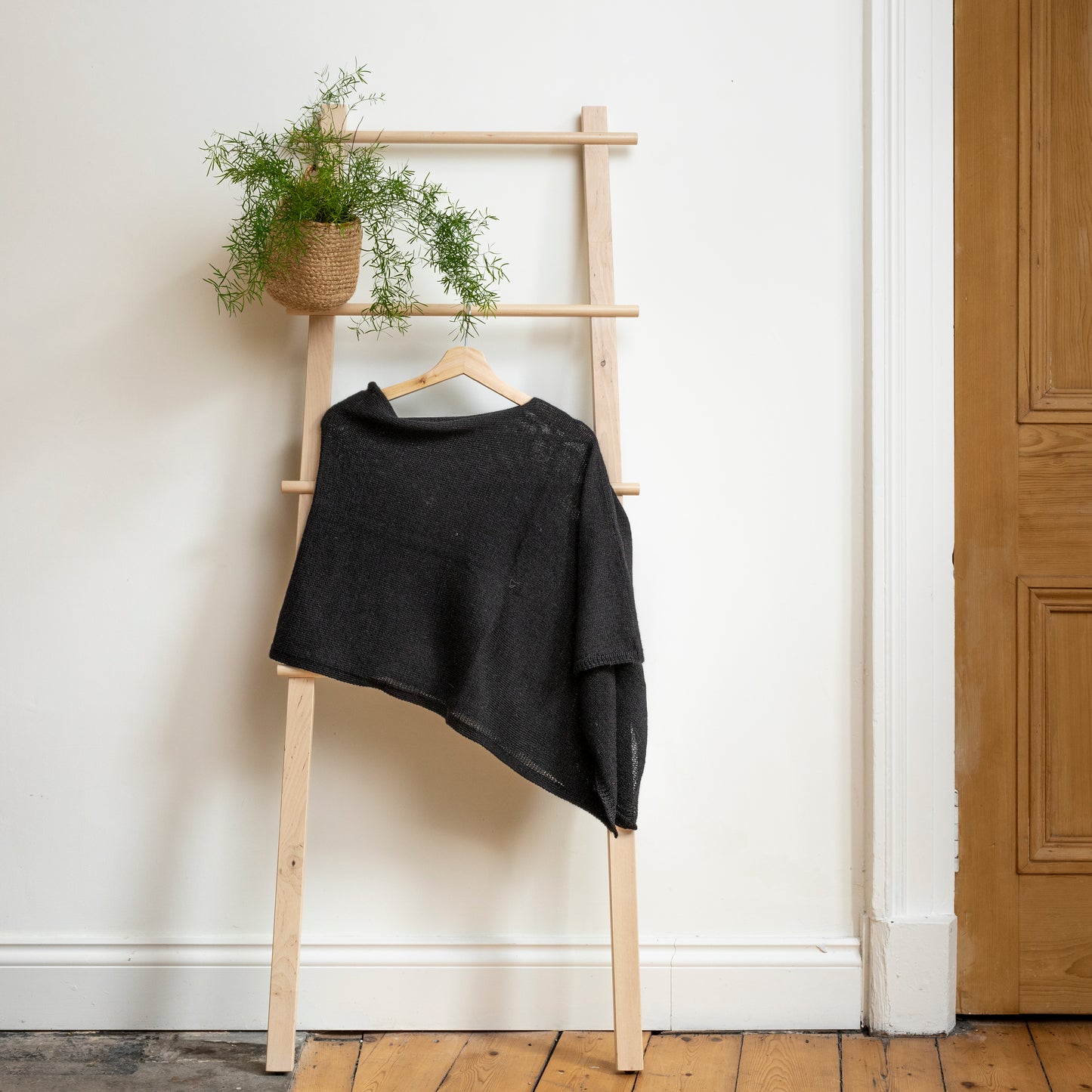 Asymmetrical charcoal luxury knitted poncho hanging on wooden ladder.