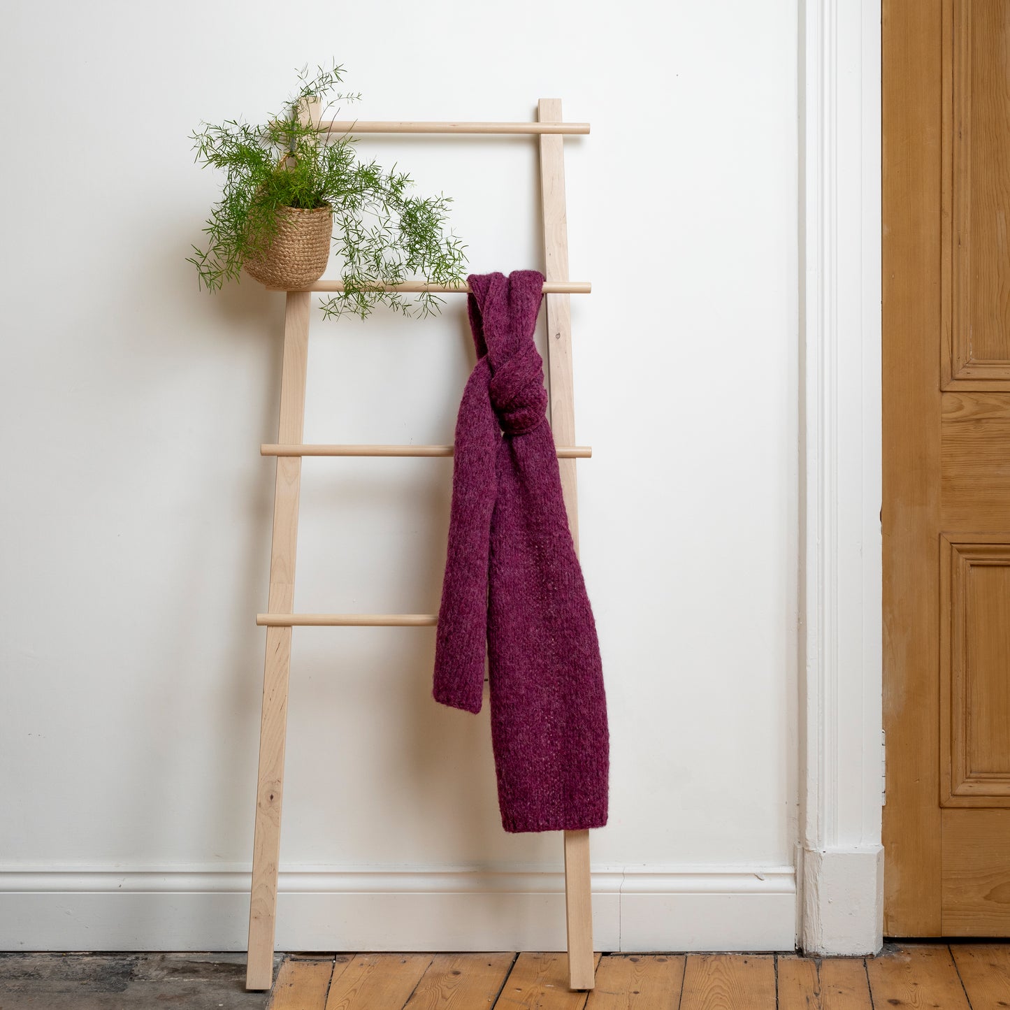 Chunky super-soft knitted scarf in colour plum hanging from wooden steps. 