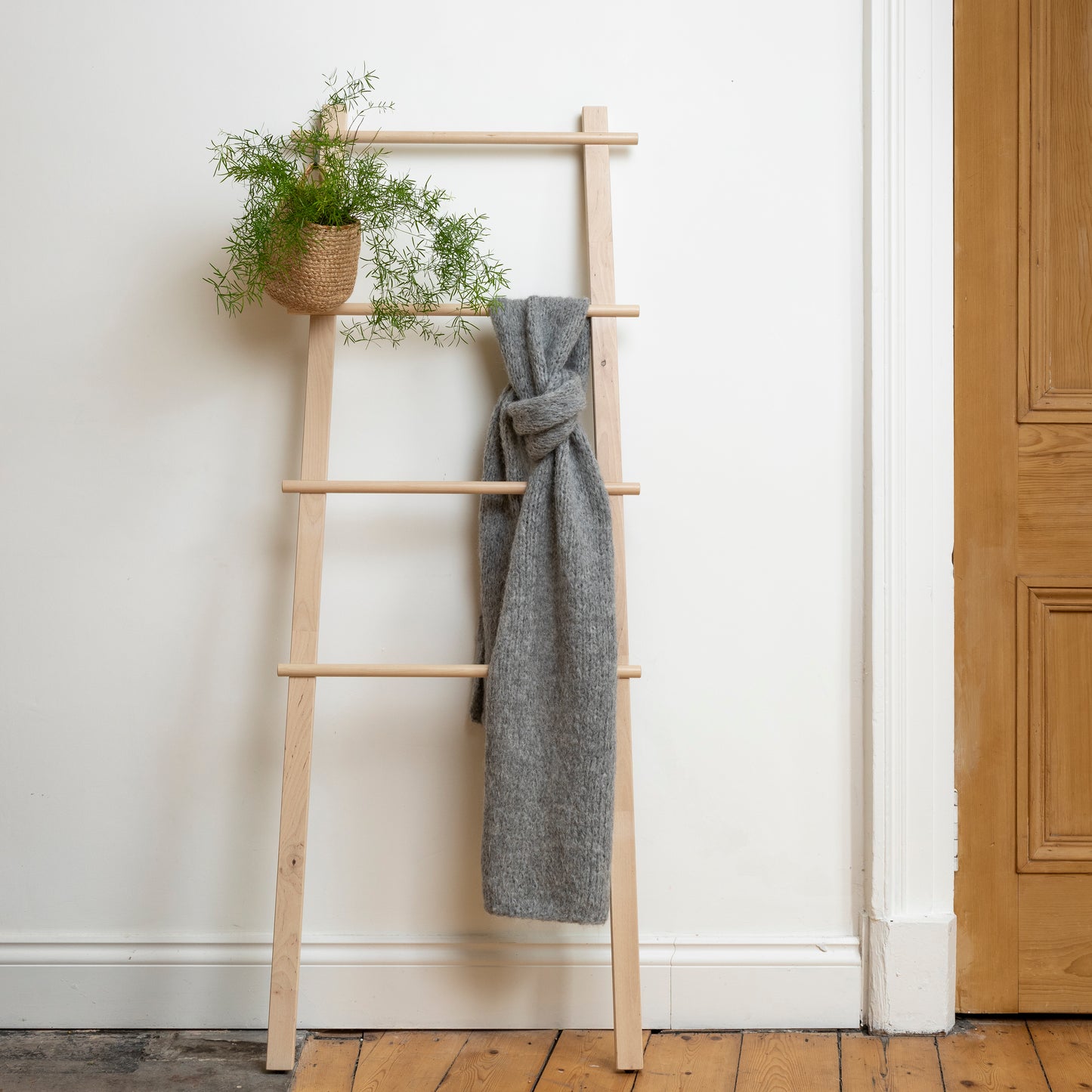 Chunky super-soft knitted scarf in colour soft grey hanging from wooden steps. 