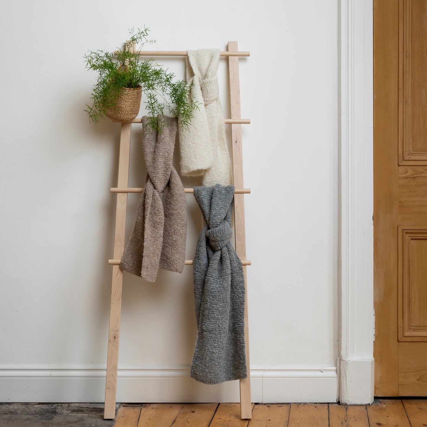 Three scarves hanging on wooden ladder. Scarves are natural, stone and oatmeal in colour. Textures are boucle, luxurious and lightweight. 