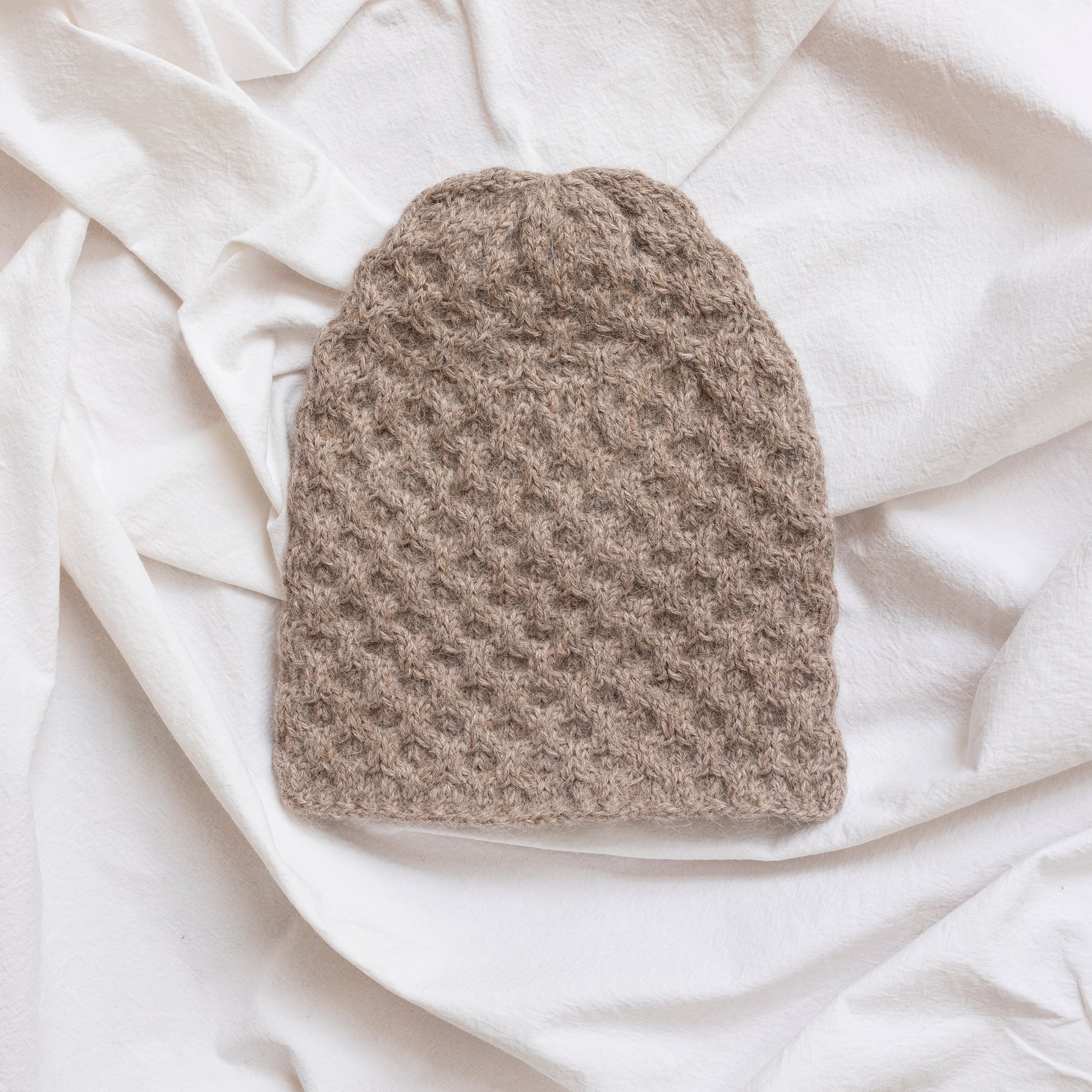 Textured hand-knitted oatmeal coloured beanie hat. 