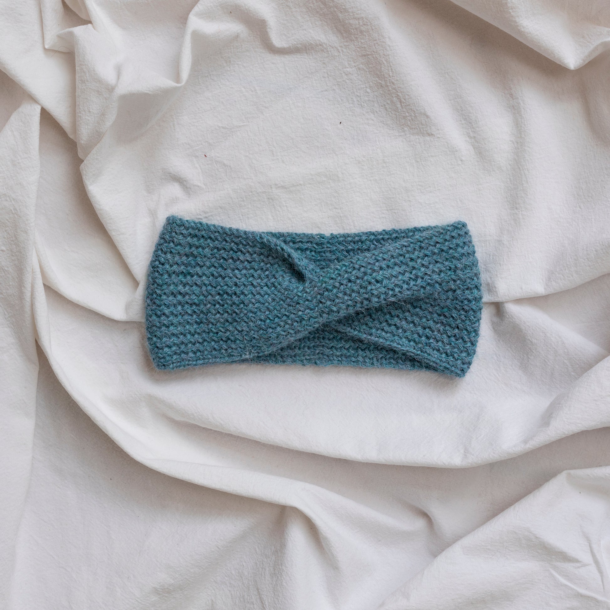 Cosy hand-knitted light blue coloured headband with a cute twist at the front. 