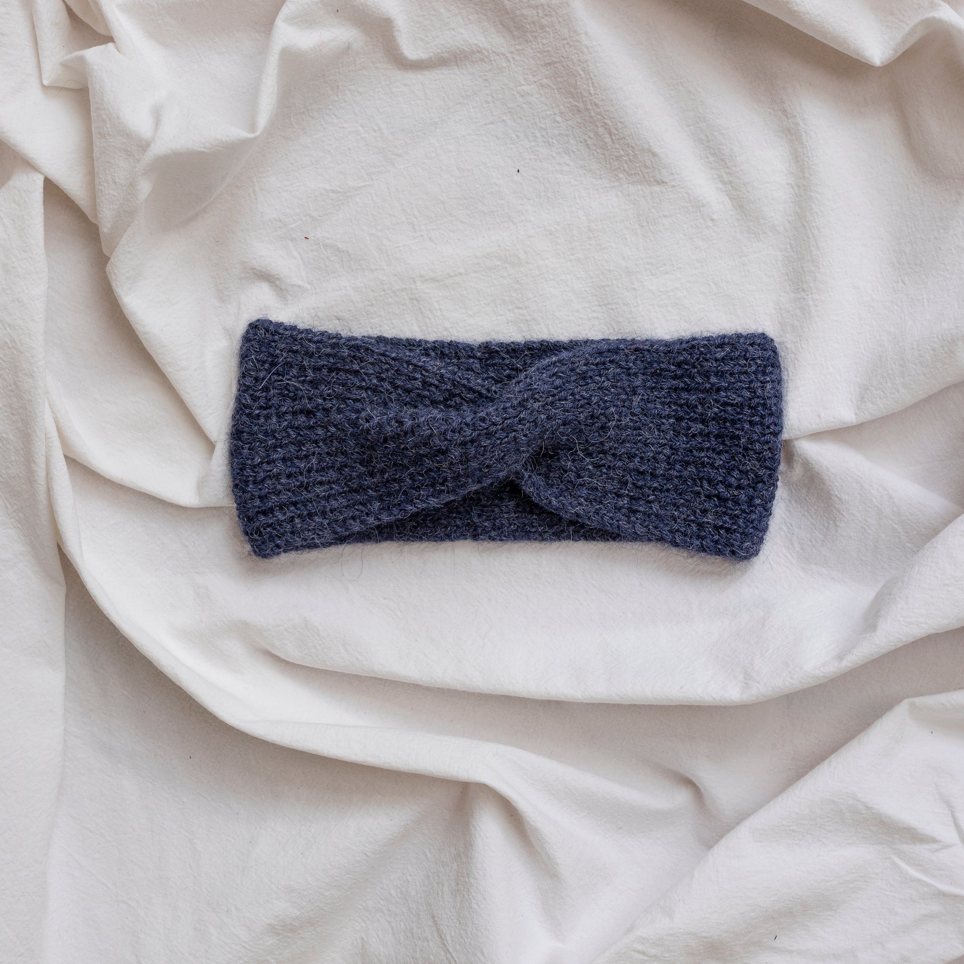 Cosy hand-knitted dark blue coloured headband with a cute twist at the front. 