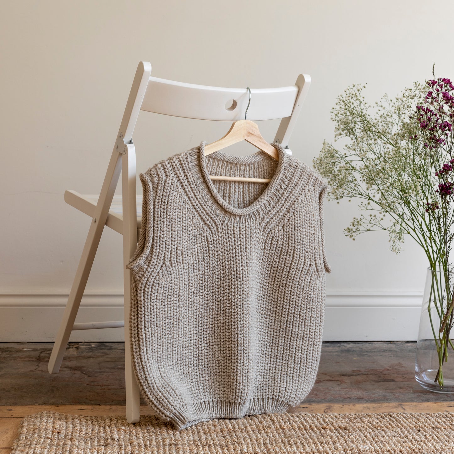 Luxury alpaca wool hand-knitted vest hanging on the back of white wooden chair. 